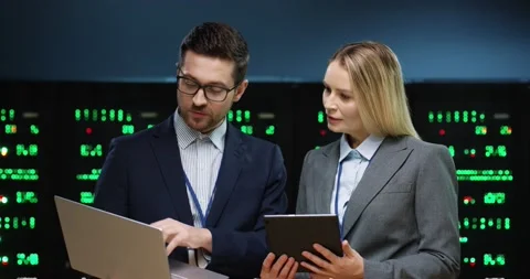 Two fellow programmers are standing in the server room. Man with glasses holding Video stock 152056262