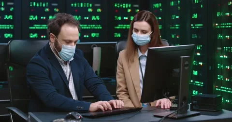 Two fellow programmers: man and woman sitting in office at desk in medical masks Video stock 145291727