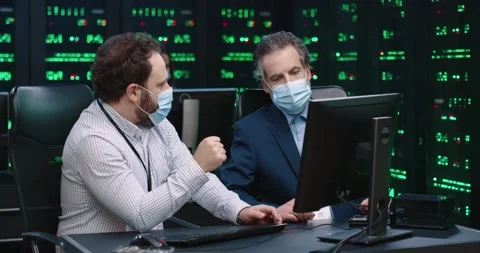 Two fellow programmers sit in office at desk in medical masks and discuss Stock Footage 145291514