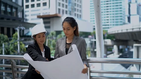Two female architects checking office blueprints on construction site Stock Footage 98339402