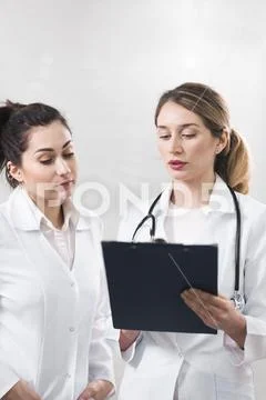 Two female assistants dressed in white coats talking to each other in the den Stock Photos
