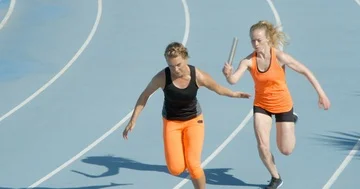 Two female athletes in Relay Race succesfully pass the baton. Stock Footage