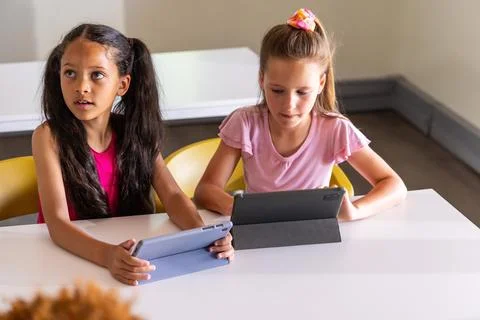 Two female children using tablets in folio cases in classroom, wearing magenta Stock Photos