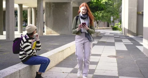 Two female classmates walking on campus path, redhead receiving notification and Stock-Footage 340454253