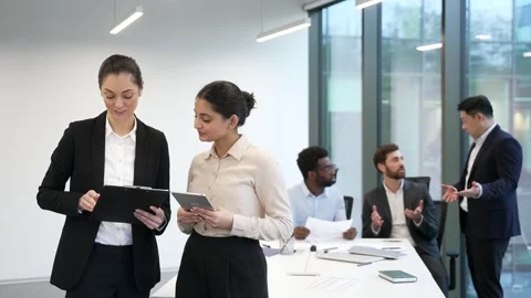 Two female co-workers communicating holding a documents and tablet standing  Stock Footage 322222277