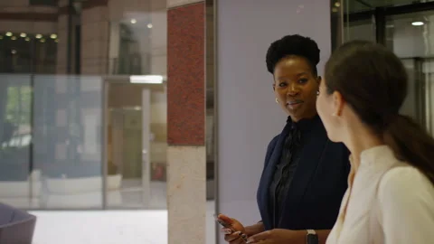 Two female colleagues exit an elevator and talk as they walk through a building  Stock Footage 243025922