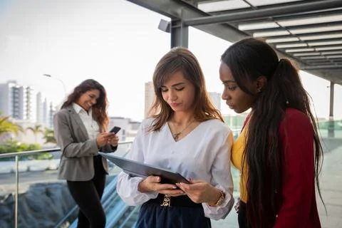 Two female colleagues work using a tablet while the other colleague in the .. Stock Photos
