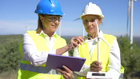 Two female engineers working with a tablet at a wind turbine farm Stock Footage 345022073