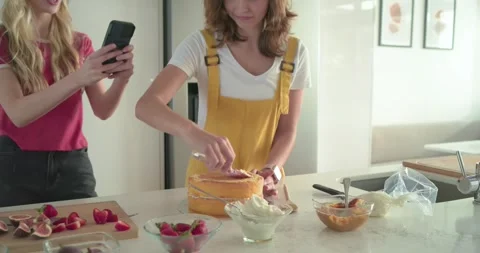 Two female friends checking recipe chopping fruit and decorating cake with Stock Footage 341240833