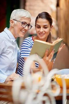 Two female friends of different generations reading a book together while the Stock Photos