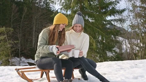 Two female friends drinking tea outside on a snowy winter day Stock Footage 285894701