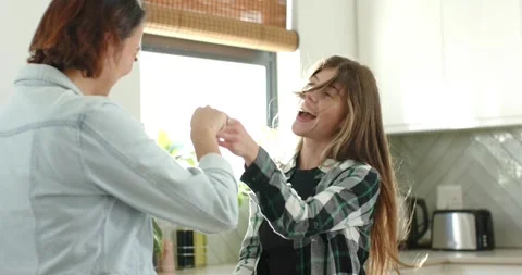 Two female friends grasping hands, spinning and tossing hair by kitchen window, Stock Footage 343515012