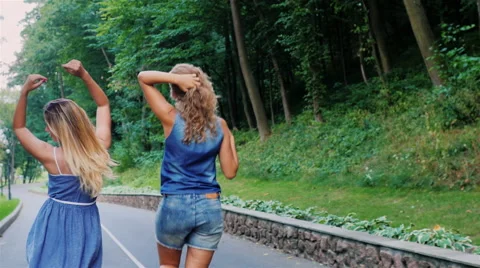 Two female friends having fun walking along the road, waving his arms, rejoicing Stock Footage 65673905