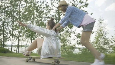 Two female friends having fun riding on longboard together Stock Footage 79793363