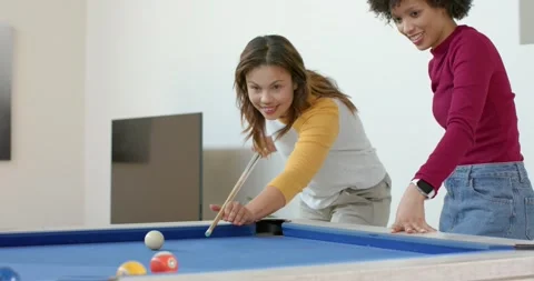 Two female friends playing pool on blue-felt table at home, cue ball striking Stock Footage 337097064