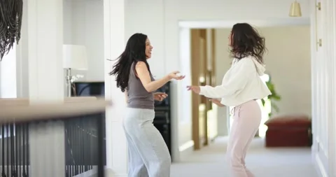 Two female friends smiling, dancing in carpeted hallway in hoodie and tank, Stock Footage 340069952