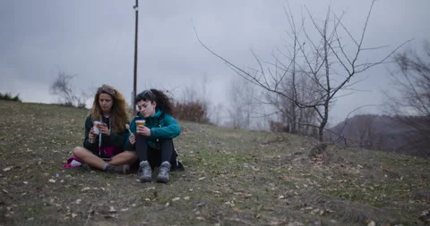 Two Female Friends Take a Break on Their Mountain Hike to Enjoy a Snack and the Stock Footage 338360947