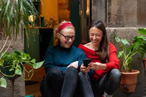 Two female friends using a smart phone, sitting together in trendy city neigh Stock Photos
