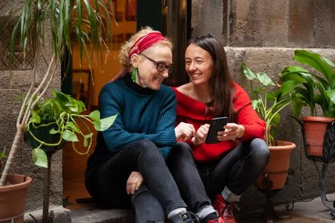 Two female friends using a smart phone, sitting together in trendy city neigh Stock Photos