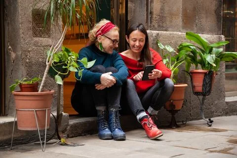 Two female friends using a smart phone, sitting together in trendy city neigh Stock Photos