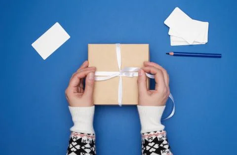 Two female hands are holding a cardboard gift square box tied with a white ri Stock Photos