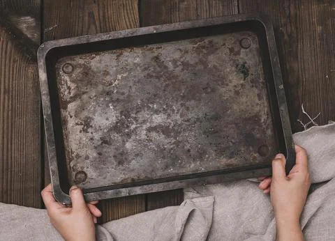 Two female hands hold a rectangular empty baking sheet on a brown wooden tabl Stock Photos