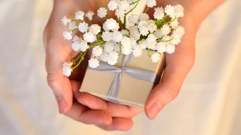 Two female hands hold a small gift box and white flowers close-up Stock Footage 119575859