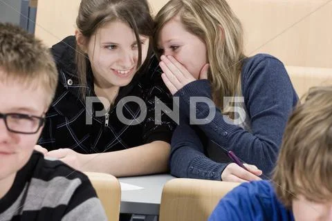 Two female high school students whispering in class Stock Photos