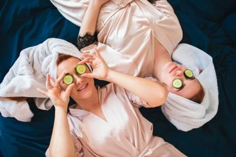 Two female models make an eye mask using fresh green cucumber. Two young women Stock Photos