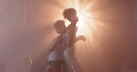Two female models posing back-to-back in studio, one wearing satin slip, strobe Stock Footage 344644089