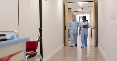 Two female nurses entering hall, walking to rounds, talking with tablet, Stock Footage 340973304
