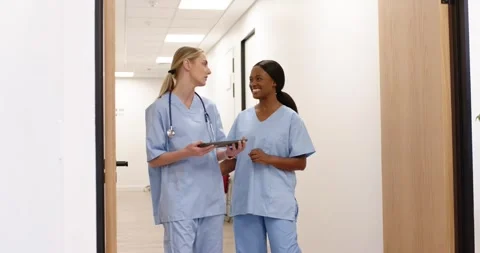 Two female nurses referencing tablet while walking and talking in clinic Stock Footage 337933018