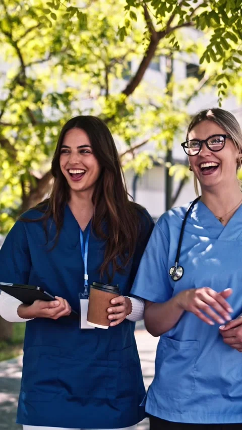 Two female nurses walking and talking during coffee break outside hospital Stock Footage 343675624