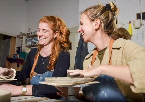 Two female potters laughing while working with clay Stock Photos