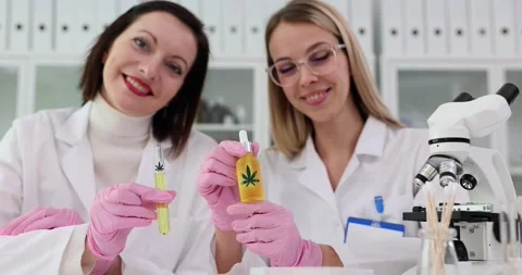 Two female scientists present a bottle with a stamp of cannabis leaves Stock Footage 270910626