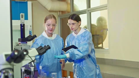 Two female scientists using a tablet and microscope in a laboratory Video stock 346939890