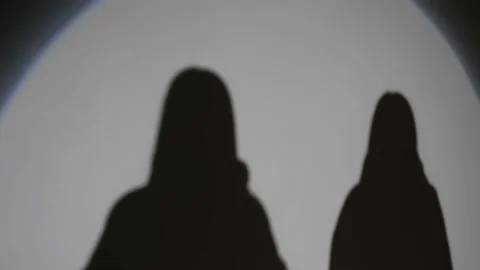 Two female shadows come out into light from spotlight and turn on each other Video stock 199256200