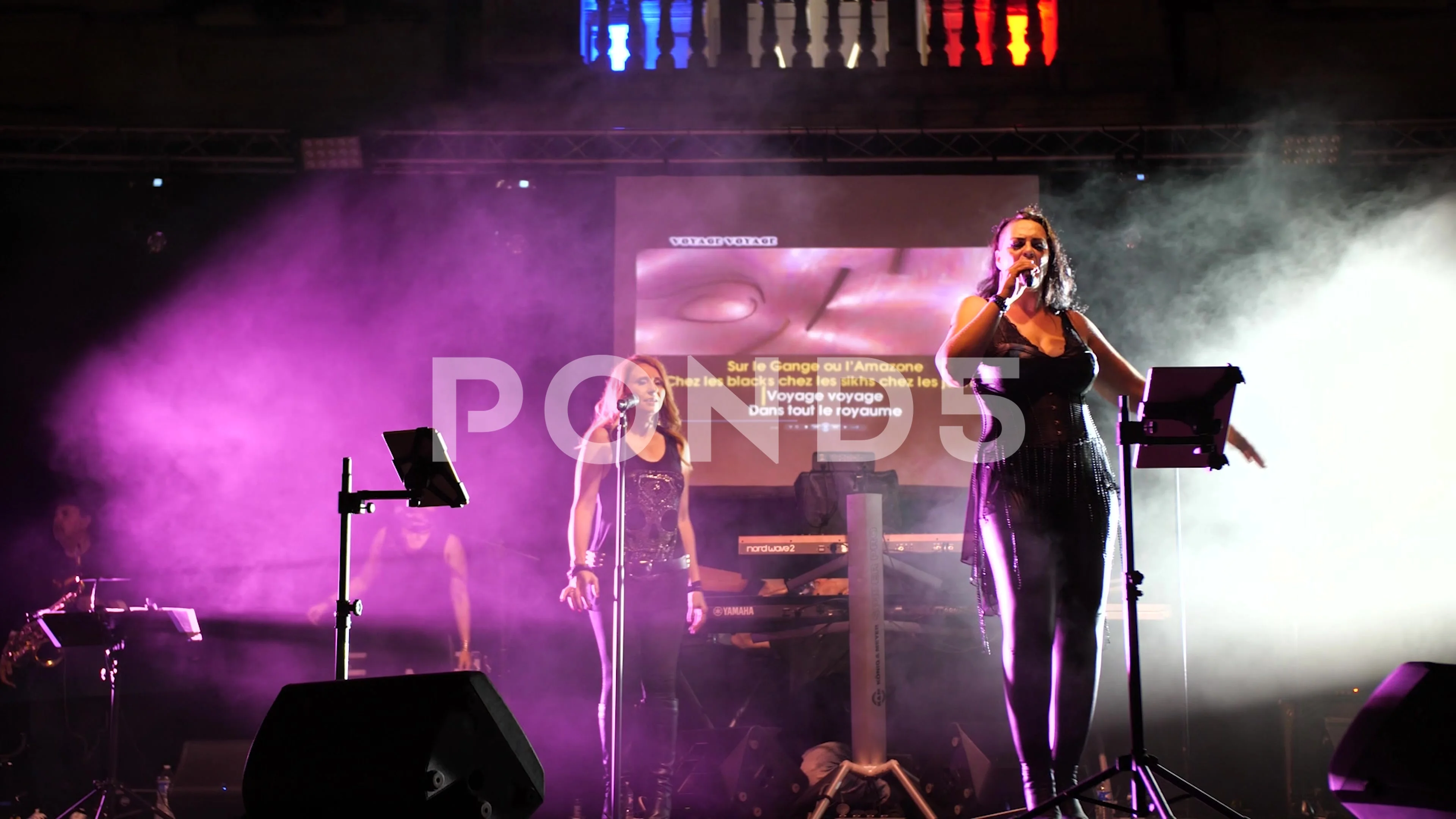 Two female singers on stage singing in purple and white smoke, one