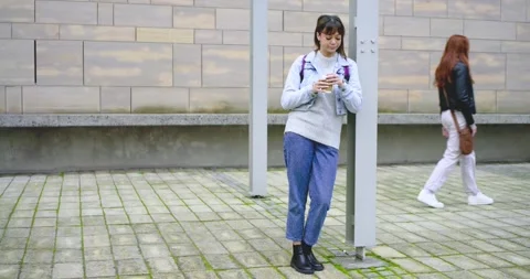 Two female strangers, walker checking bag, woman leaning on metal post sipping Stock Footage 336957357