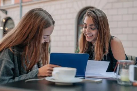 Two female students are learning and talking at the outdoor cafe restaurant. Stock Photos