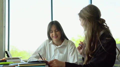 Two female students sitting by desk in lecture hall and discussing passage in Stock Footage 243323997