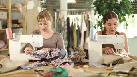 Two female tailors are sitting at a table in the workshop and sewing clothes on Stock Footage 341427655