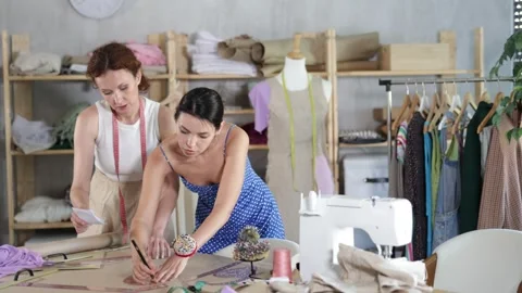 Two female tailors draws pattern on a sheet of paper in a sewing workshop Stock Footage 332639969