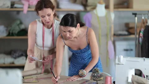Two female tailors draws pattern on a sheet of paper in a sewing workshop Stock Footage 341427477