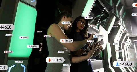 Two female technicians examining floating data icons on tablet in control room, Stock Photos