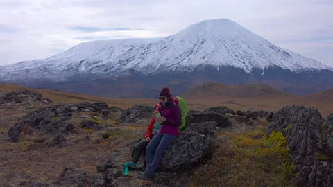 Two female travelers with backpacks sit on the stones and eat nuts Stock Footage