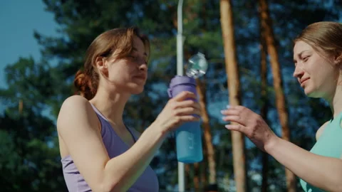 Two female twins drinking water after outdoor workout Видео 336960882