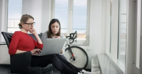Two female workers talking about website on laptop in a bright location Video stock 91987808