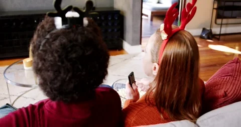 Two females extending remote, sharing popcorn, wearing antlers, watching Stock Footage 344229089