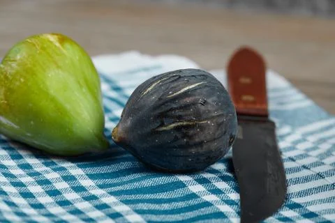 Two figs and a knife with a blue tablecloth on wooden table Stock Photos